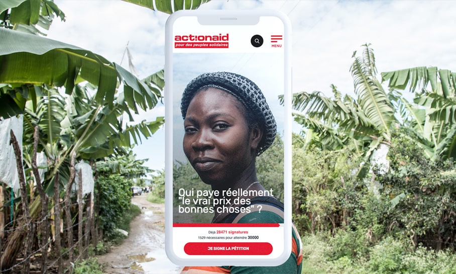 Image conceptuelle d'un énorme smartphone s'intégrant dans un paysage rural avec des bananiers. Sur l'écran, une campagne d'ActionAid présente le portrait d'une femme avec le texte 'Qui paye réellement le vrai prix des bonnes choses ?'. L'écran affiche également le nombre de signatures collectées pour une pétition. La juxtaposition de la technologie moderne avec l'environnement naturel évoque un message sur l'impact social et économique de l'agriculture mondialisée.