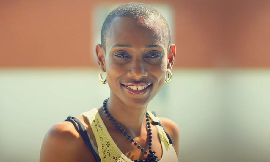 Portrait de Ghislaine, souriante portant un collier noir et des boucles d'oreilles dorées, habillée d'un débardeur beige, photographie prise en gros plan.