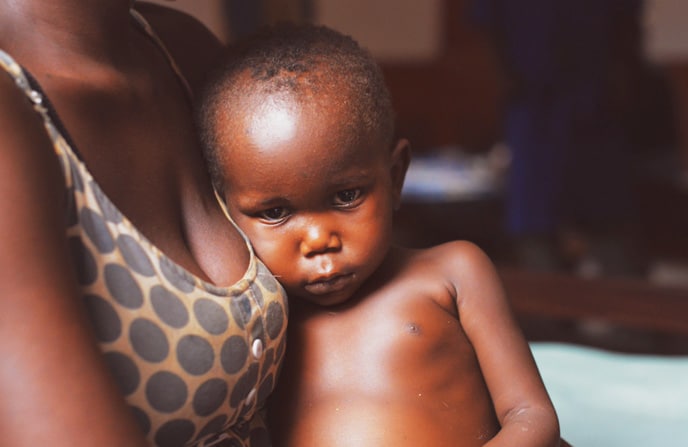 Enfant centrafricain pensif tenu tendrement par sa mère à l'hôpital pédiatrique de Bangui, exprimant une émotion profonde et la relation parent-enfant dans un contexte de guerre civile.