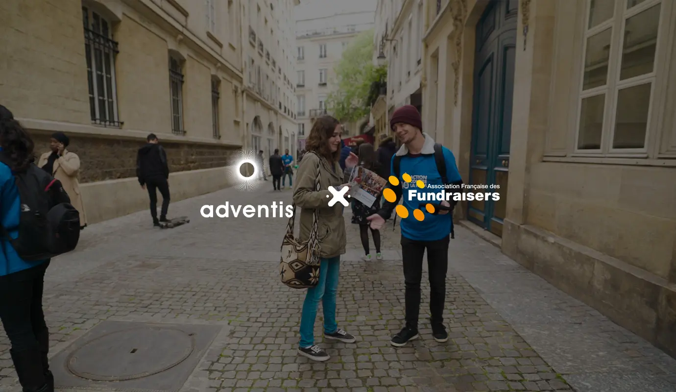 Deux jeunes, un homme et une femme, s'engagent dans une conversation animée dans une rue animée près de bâtiments historiques, où est réalisée une collecte de fonds. Les logos d'Adventis et de l'Association Française des Fundraisers sont visibles au premier plan, illustrant leur partenariat pour la promotion du fundraising.